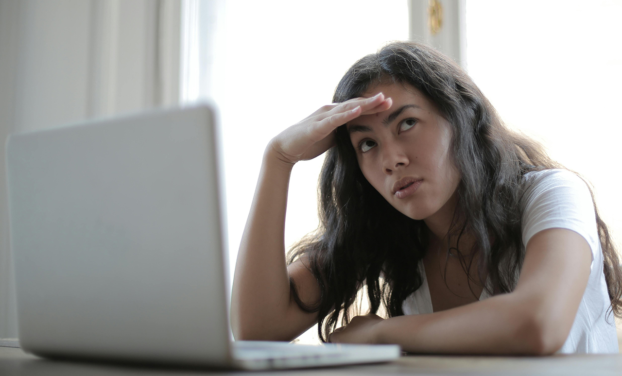 Photo of an unhappy woman sitting at a desk with a laptop.